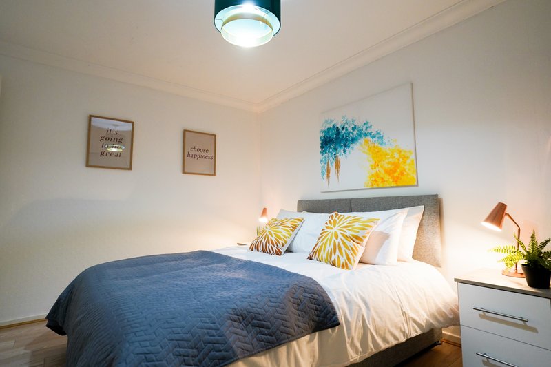 Bedroom with double bed, blue bedding, yellow accent pillows, and framed wall art