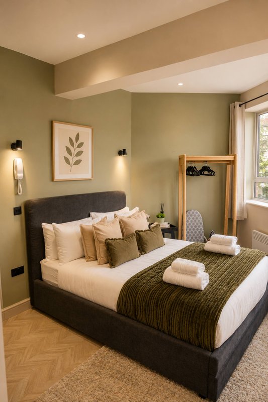 Bedroom with double bed, green walls, framed botanical print, and natural lighting from window
