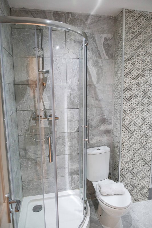 Modern bathroom with curved glass shower enclosure, toilet, and patterned tile walls