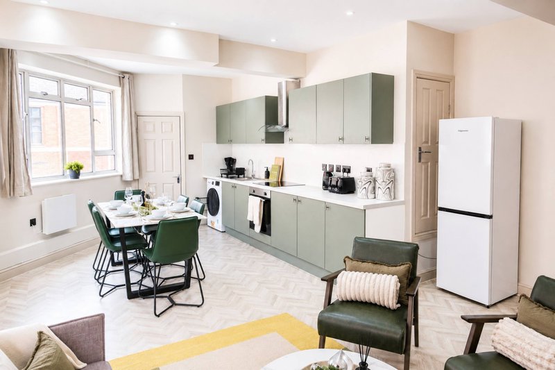 Open-plan kitchen and dining area with sage green cabinets, white appliances, dining table and green chairs