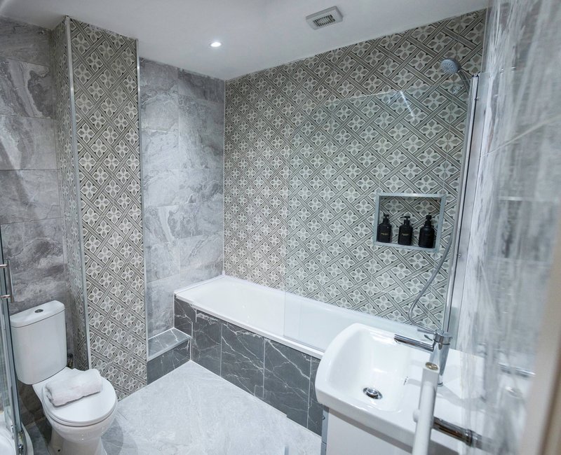 Modern bathroom with patterned tile walls, white toilet, bathtub and walk-in shower