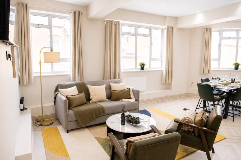 Bright modern living room with grey sofa, round coffee table, armchairs, floor lamp and dining area