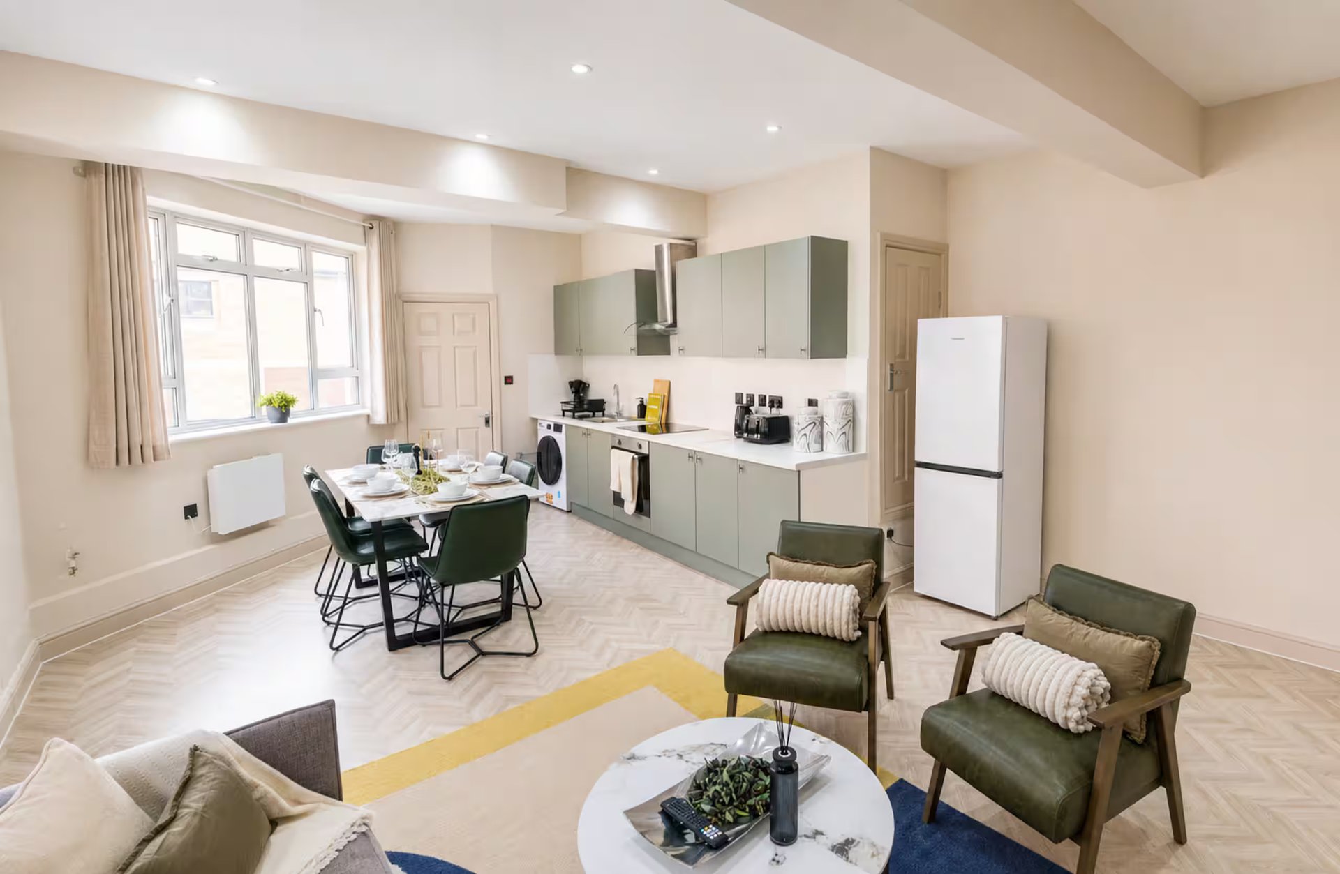 Open-plan kitchen and living area with dining table, green armchairs, and modern appliances