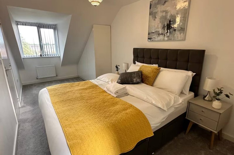 Bright bedroom with double bed, yellow bedding, dark headboard, and window with garden view