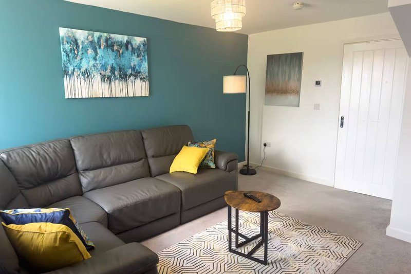 Living room with grey leather sofa, teal accent wall, wooden side table and yellow accent pillows