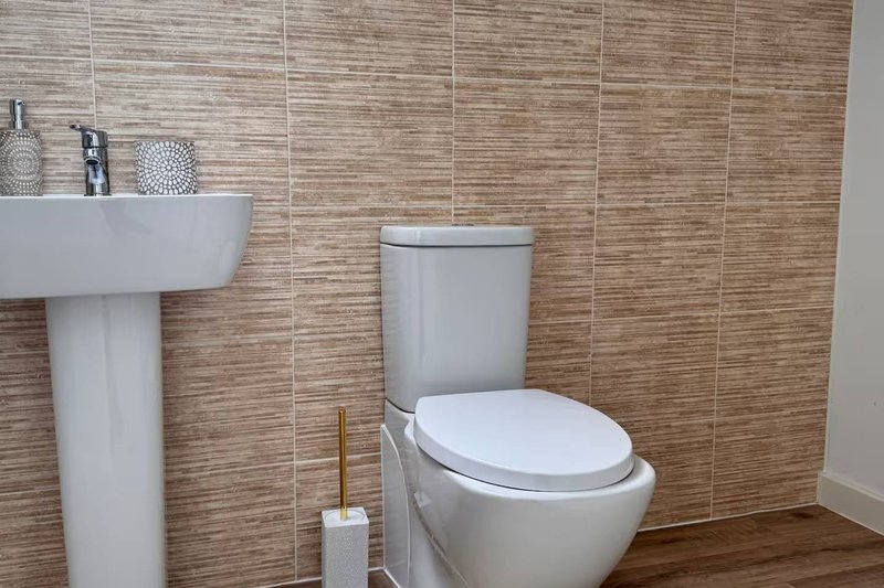 Modern bathroom with wood-effect tiles, white pedestal sink, toilet, and brass accessories