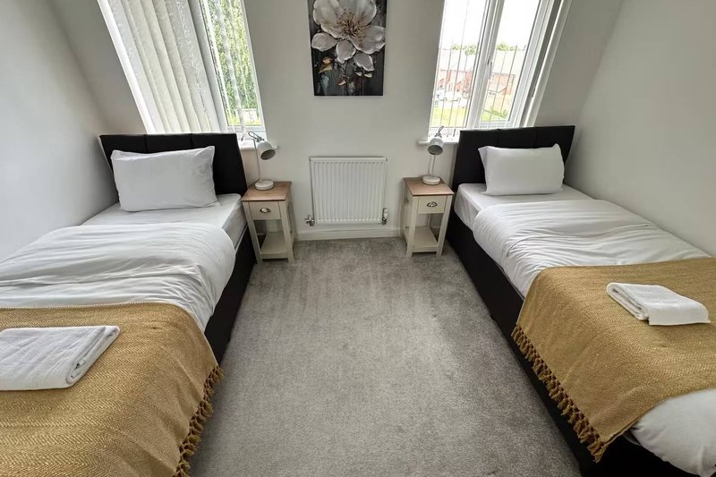 Twin bedroom with two single beds, bedside tables, radiator and window with curtains