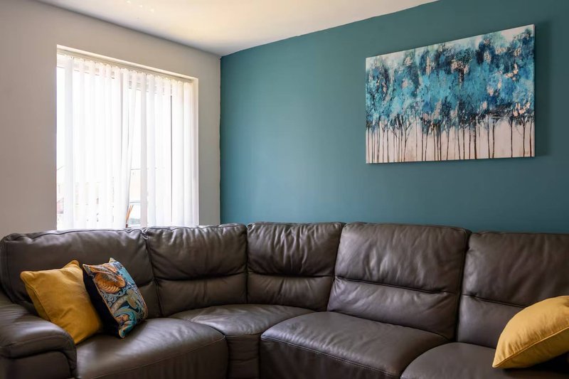Living room with brown leather sectional sofa, yellow cushions, and landscape artwork on teal wall