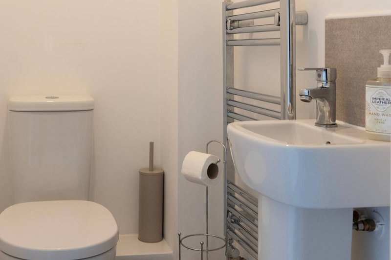 Modern bathroom with toilet, pedestal sink, heated towel rail and white walls