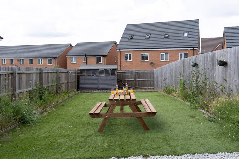 Rear garden with lawn, wooden picnic tables, fencing and brick terraced houses beyond