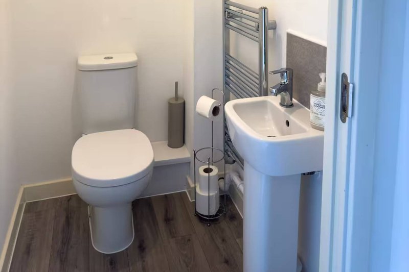Small bathroom with toilet, pedestal sink, heated towel rail and wooden flooring