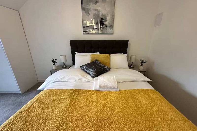 Modern bedroom with double bed, yellow bedding, black headboard and bedside lamps