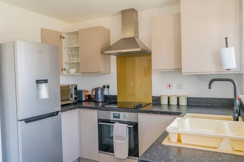 Modern kitchen with white cabinetry, stainless steel appliances, dark countertop and yellow splashback