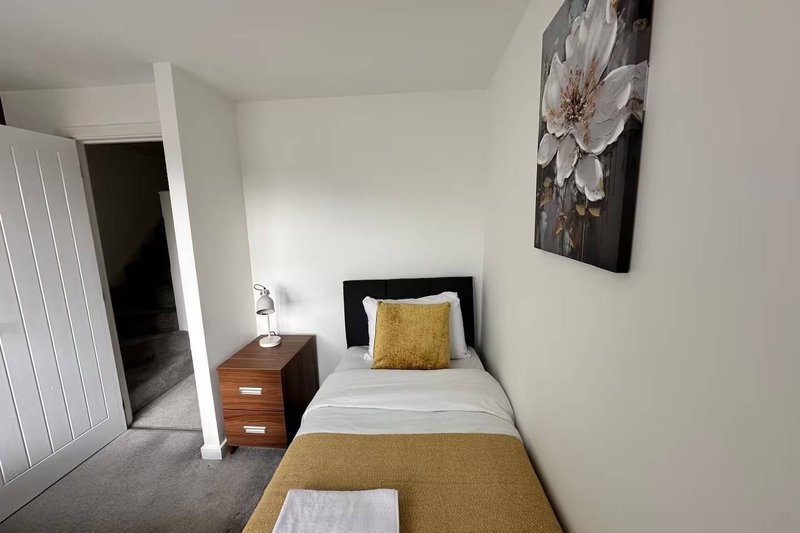 Compact bedroom with single bed, wooden nightstand, white bedding and yellow cushion