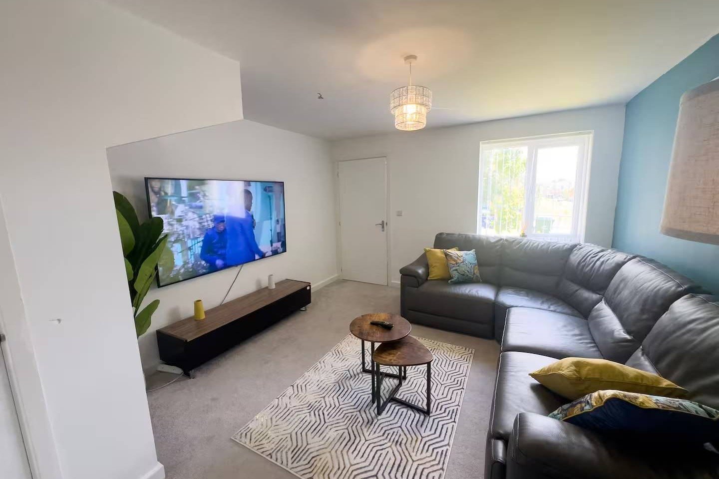 Modern living room with grey sectional sofa, wall-mounted TV, geometric area rug and pendant light