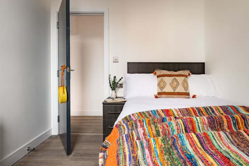 Modern bedroom with double bed, colorful striped blanket, black headboard and bedside table
