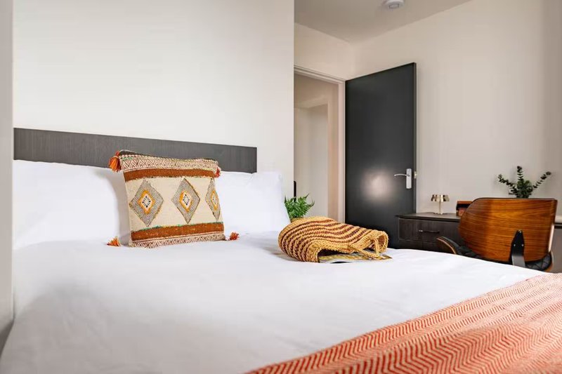Modern bedroom with white bed, decorative pillows, wooden dresser, and black door