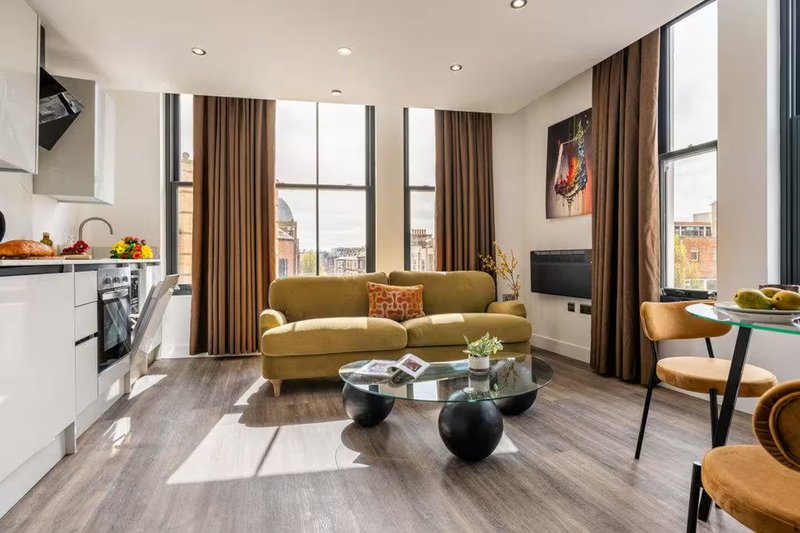 Open-plan living area with mustard sofa, kitchen, dining chairs and city views