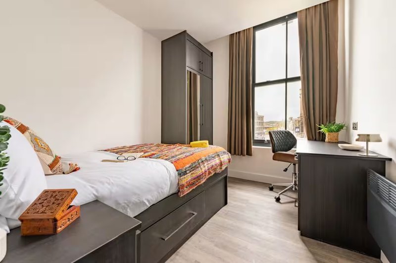 Modern bedroom with single bed, dark wood furniture, desk area and large window with city view