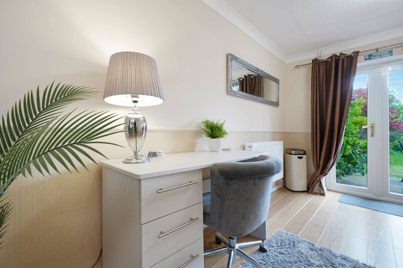 Modern home office with white desk, grey chair, potted plants and garden view doors