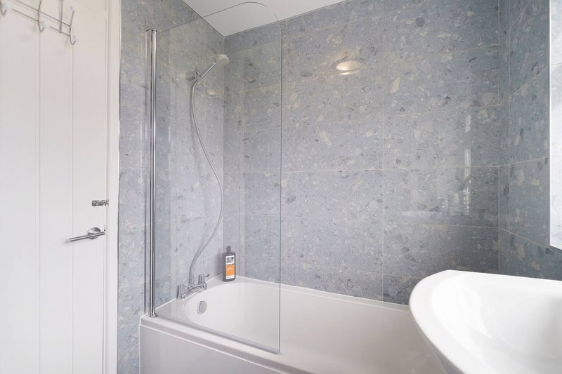 Modern bathroom with grey tile shower enclosure, white bathtub and toilet