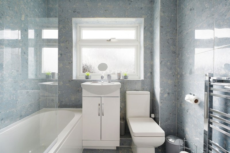 Modern bathroom with bathtub, white vanity, toilet, heated towel rail and window