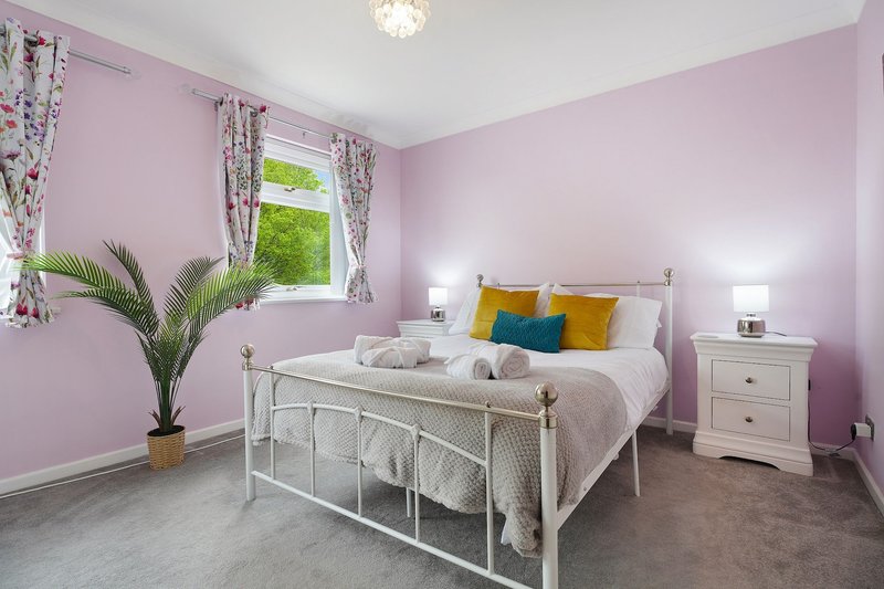 Pink bedroom with white metal bed frame, cream bedding, colorful cushions, potted plant and window