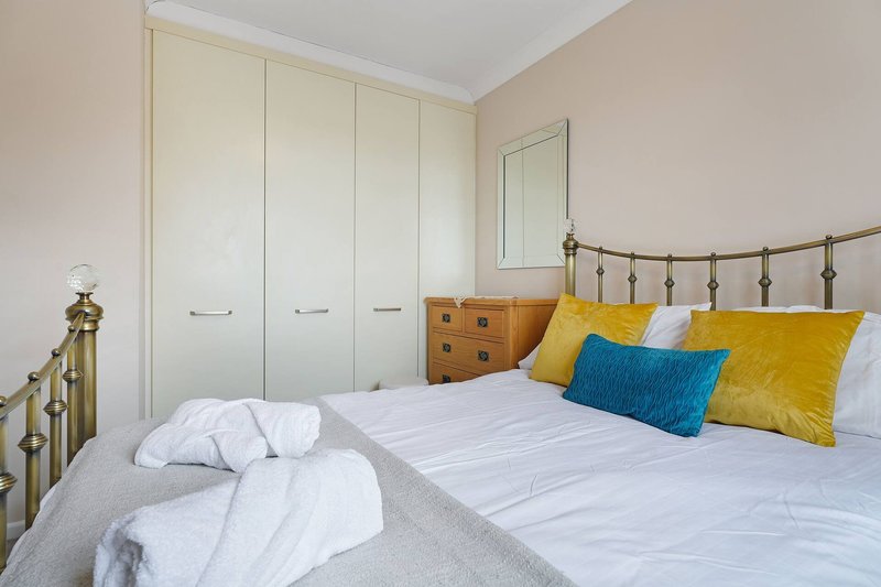 Bright bedroom with double bed, brass headboard, white wardrobe, yellow and blue cushions