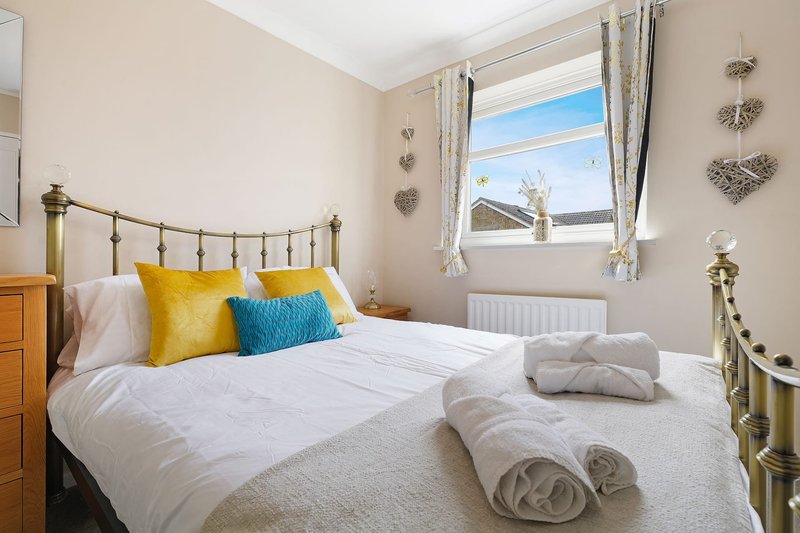 Bright bedroom with double bed, yellow and blue cushions, rolled towels, and window with countryside view