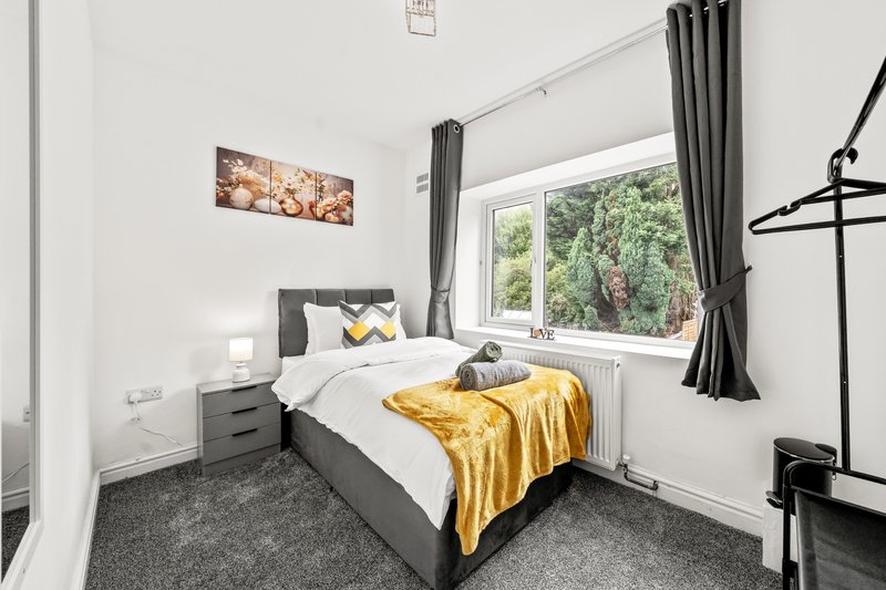 Bright modern bedroom with grey bed, yellow throw, white bedding, and large window with garden view