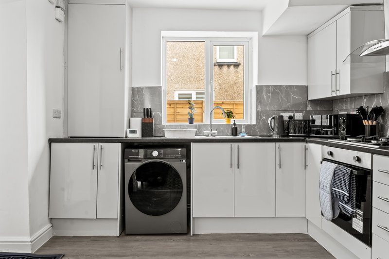 Modern kitchen with white cabinetry, black washing machine, gas range, and window overlooking garden
