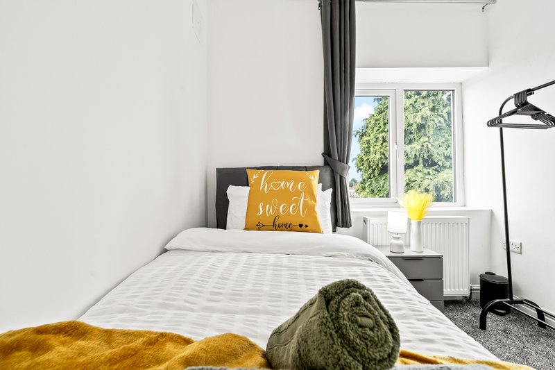 Bright bedroom with single bed, yellow and green throws, decorative pillow, and window overlooking garden