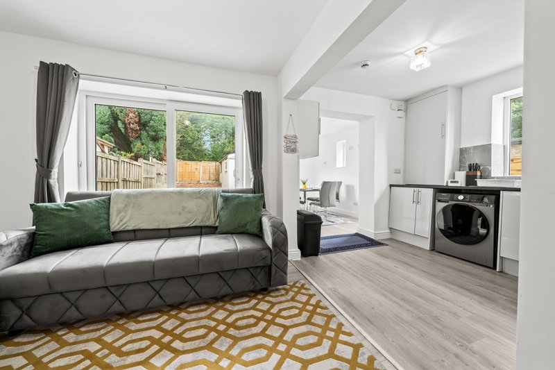 Open-plan studio with grey sofa, green cushions, wooden flooring, kitchenette and garden view