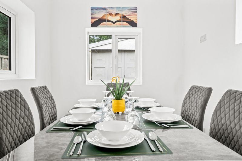 Modern dining room with grey quilted chairs, set table, and framed artwork above window