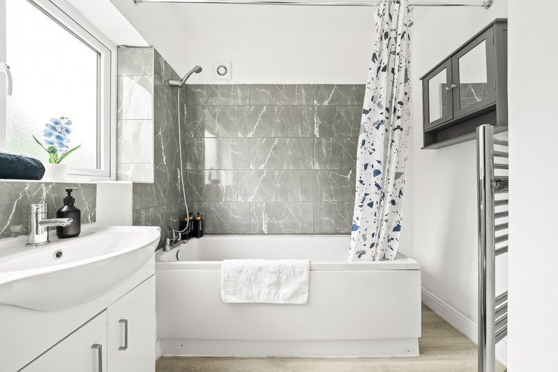 Modern bathroom with white bathtub, marble tile surround, sink, and blue floral shower curtain