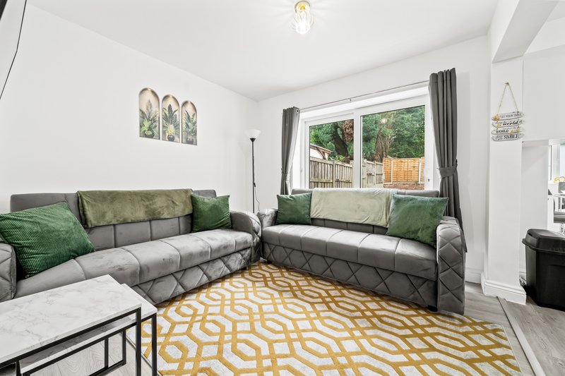 Bright living room with grey corner sofa, green cushions, yellow patterned rug and garden view