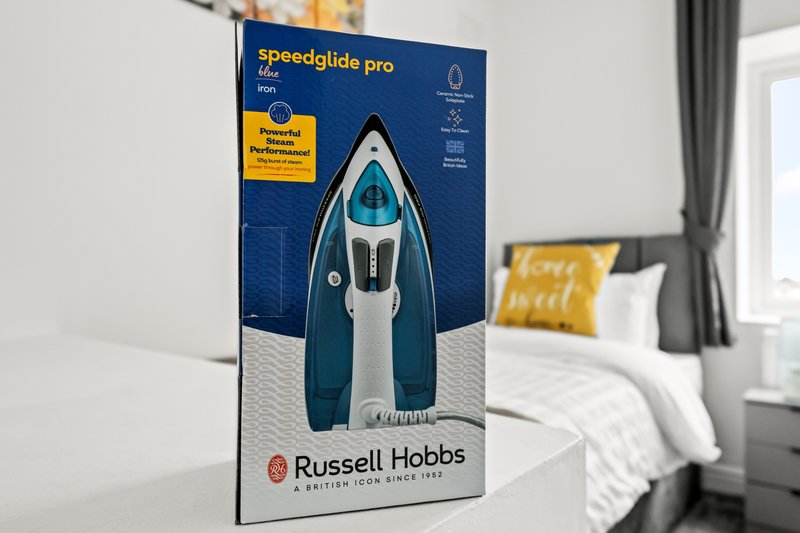 Bedroom with double bed, boxed steam iron on nightstand, window with grey curtains