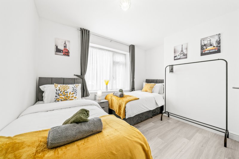Bright bedroom with two single beds, yellow bedding, grey headboards and window with curtains