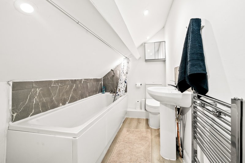 Modern bathroom with white bathtub, marble-effect splashback, toilet, sink and heated towel rail