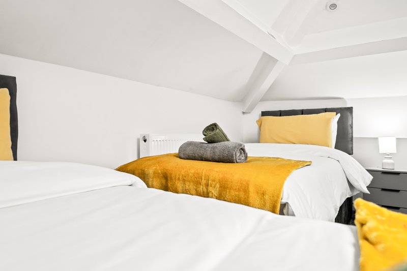 Modern bedroom with two single beds, yellow accents, white walls and sloped ceiling