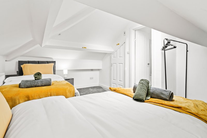 Bright attic bedroom with two beds, yellow bedding, white walls and sloped ceiling