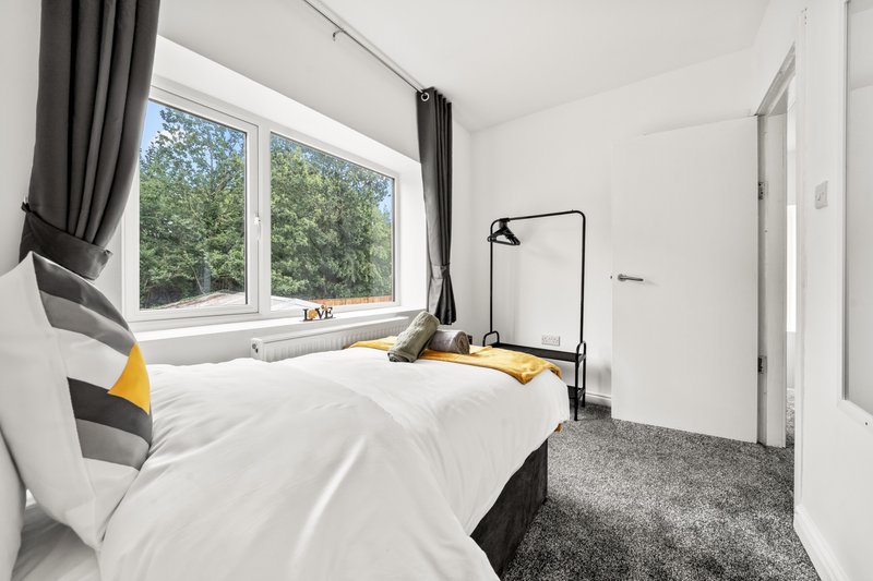 Bright bedroom with double bed, large window, black frame mirror and grey carpet flooring