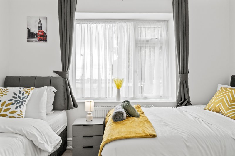 Modern bedroom with two beds, grey headboards, white bedding, yellow accents and large windows