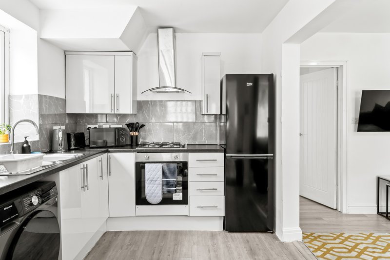 Modern kitchen with white cabinets, black appliances, gray tile backsplash and wooden flooring