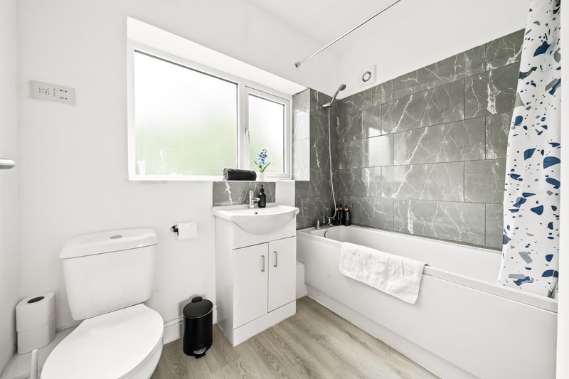 Modern bathroom with white toilet, vanity unit, bathtub, grey tile walls and window