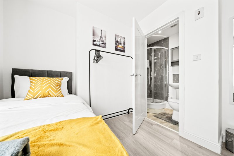 Bright bedroom with single bed, yellow bedding, wall art, and ensuite bathroom visible through open door