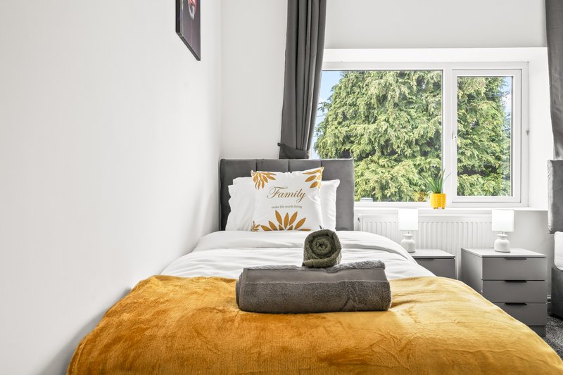 Bedroom with single bed, yellow bedspread, decorative pillow and window overlooking garden