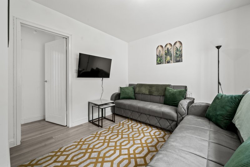 Modern living room with gray sofa, green cushions, mounted TV, and patterned rug