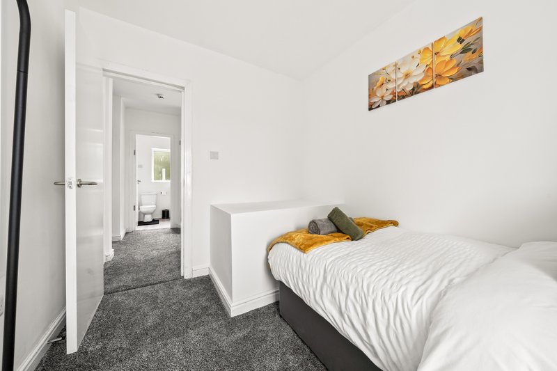 Modern bedroom with single bed, white headboard, yellow accent pillow, and open doorway to hallway