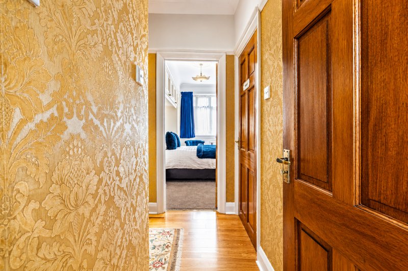 Hallway with gold damask wallpaper, wooden doors, and view into bedroom with blue upholstered furniture